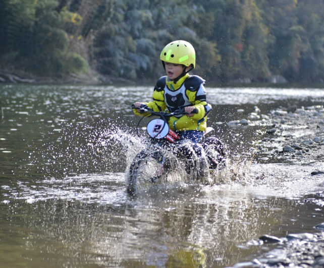 子供がモトバイクに乗って水たまりを走っている様子